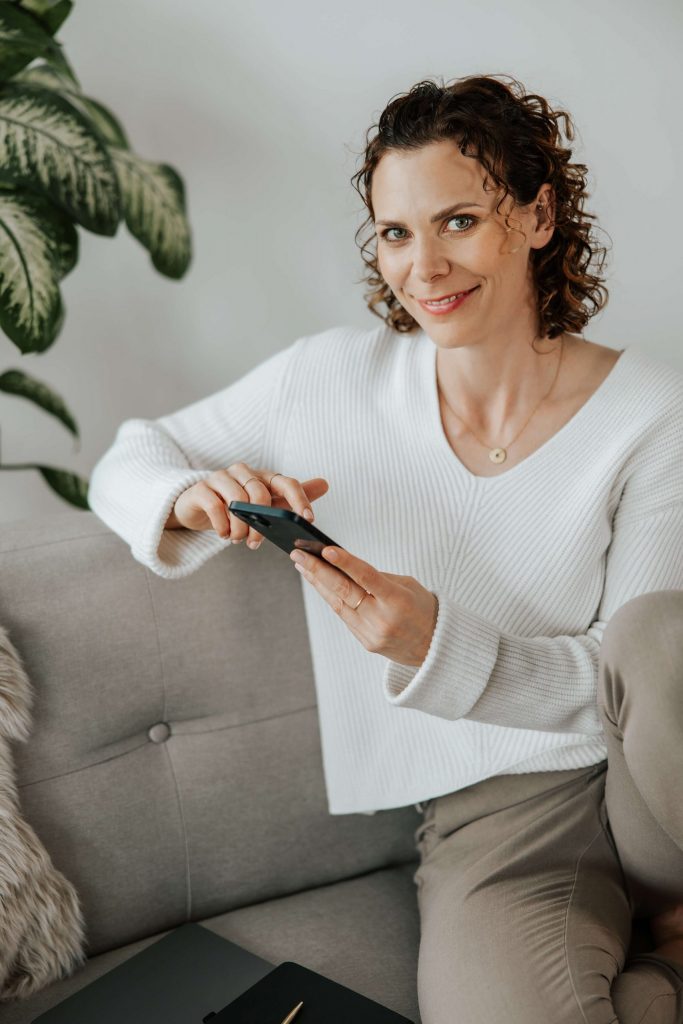 Andrea blickt lächelnd zur Seite, während sie ihr Handy in der Hand hält. Präsent, zugewandt, klar.