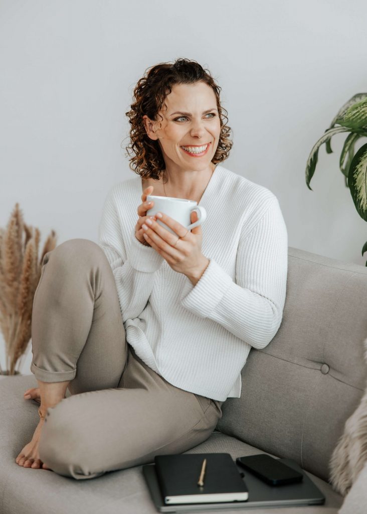 Andrea lächelt strahlend mit einer Tasse Kaffee in der Hand – Momente echter Lebensfreude und Leichtigkeit.