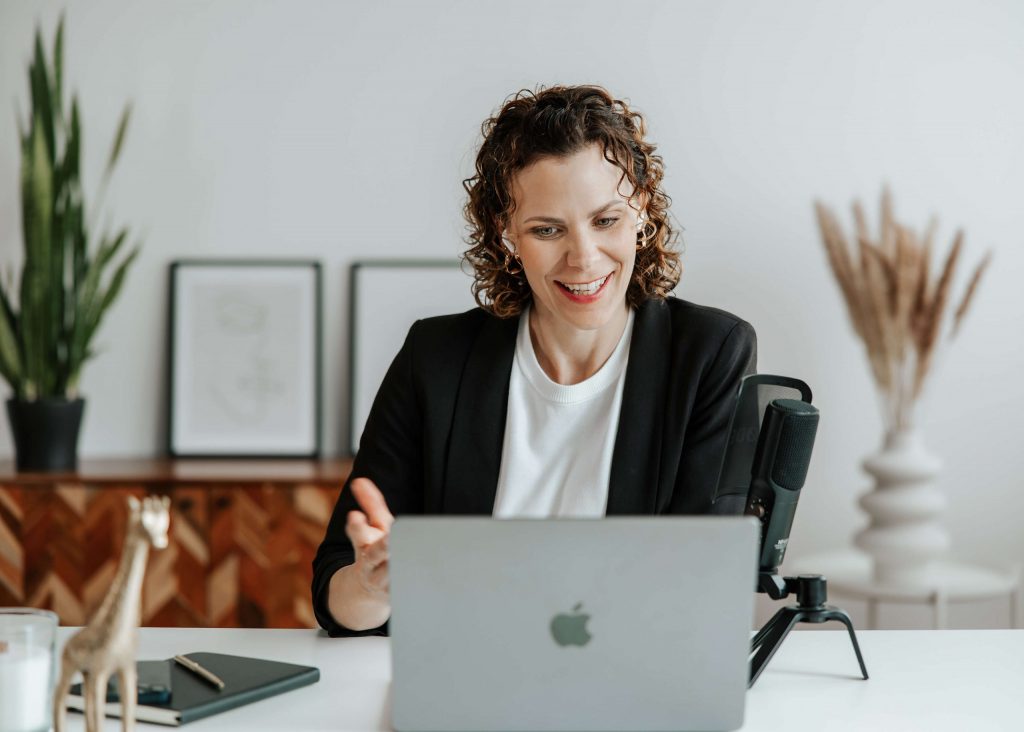 Andrea blickt lächelnd auf den Laptop, Mikrofon und Dekoration schaffen eine professionelle Atmosphäre.