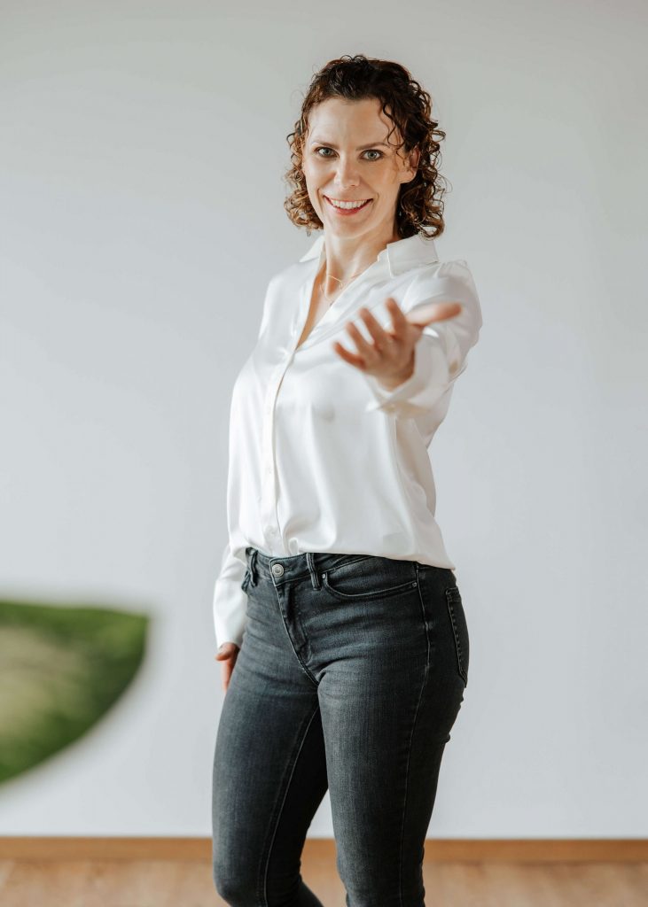 Andrea Görlich lächelt in die Kamera und streckt einladend die Hand nach vorne, ein Symbol für Verbindung und Aufbruch.