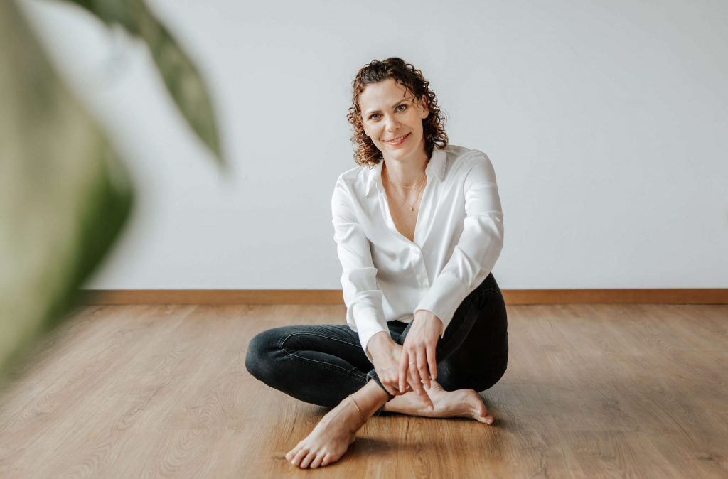 Andrea Görlich sitzt auf dem Boden, schaut freundlich in die Kamera und wirkt offen und einladend.